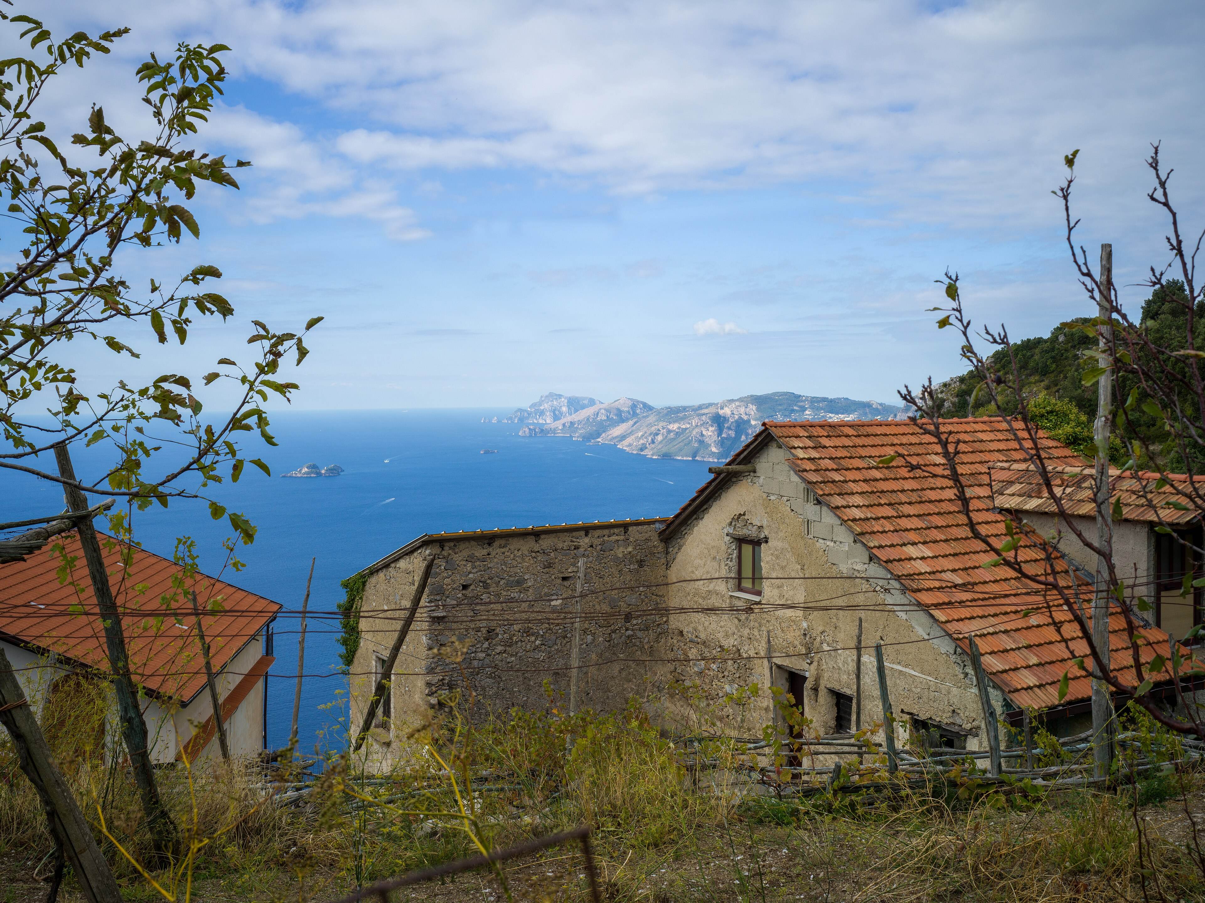Old stone farmhouses with tiled roofs beside the path, the sea and Capri in the distance