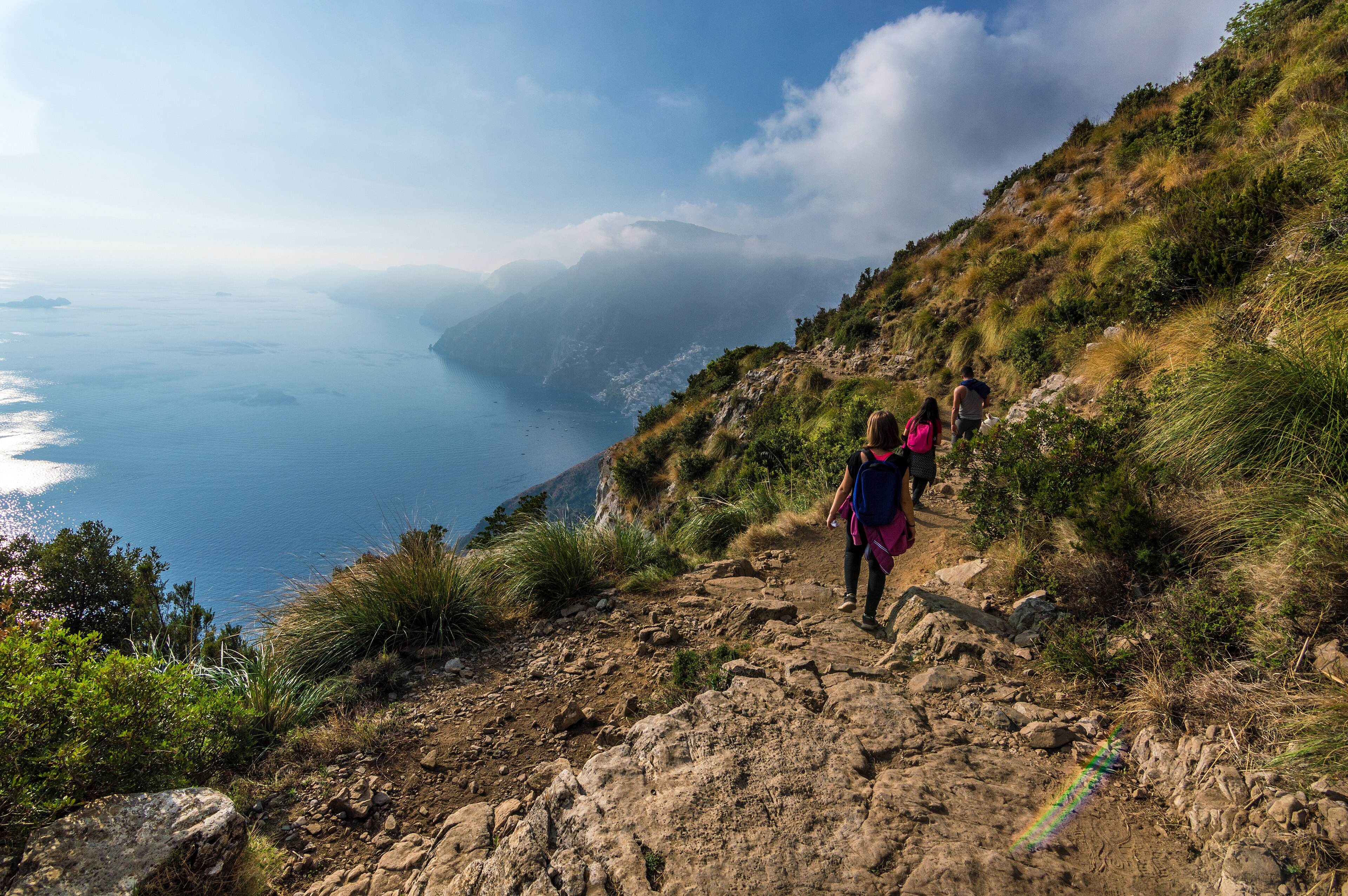 Walkers heading along a stony stretch of the trail, the sea and hazy headlands beyond